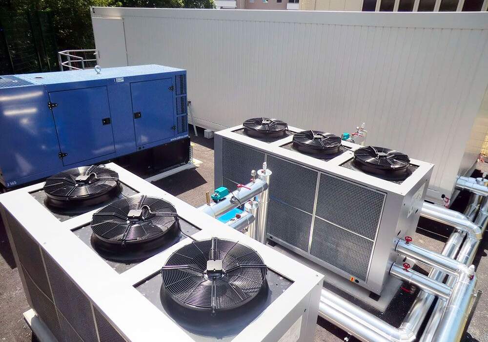 Système de climatisation sur toit avec plusieurs groupes réfrigérants et un générateur, entouré de bâtiments.