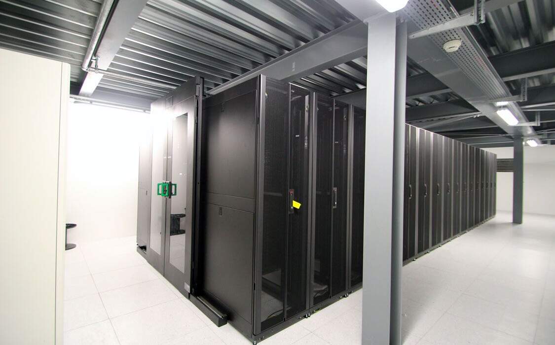 Système de serveurs avec rangées de racks noirs dans un espace intérieur moderne, éclairé par des lumières blanches.