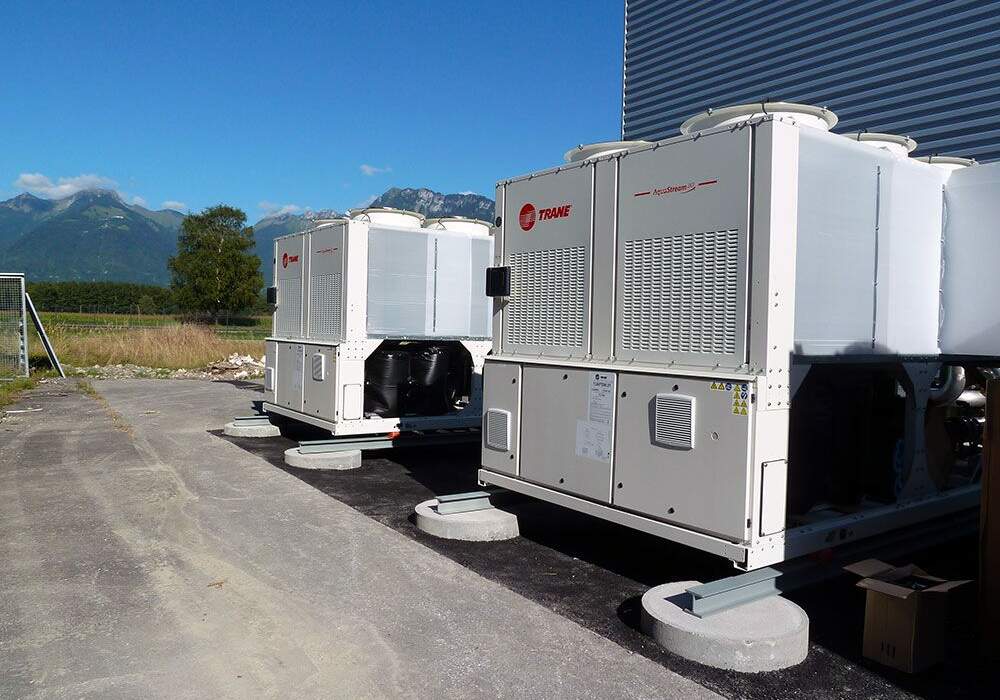 Deux unités de refroidissement sur un sol en béton, avec des montagnes verdoyantes et un ciel bleu en arrière-plan.