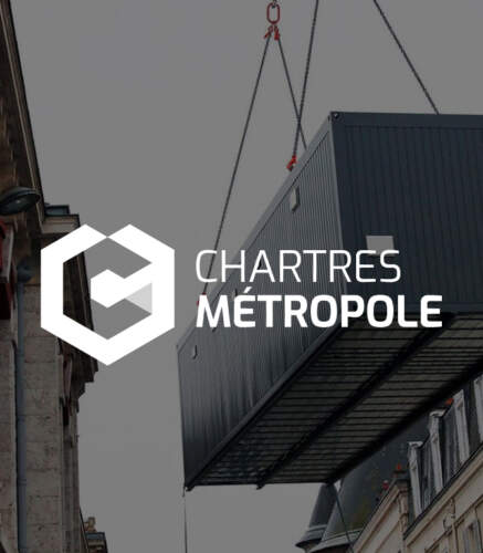 Conteneur noir suspendu par une grue sur un bâtiment en pierre, avec le logo 