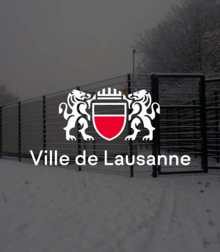 Panneau de la Ville de Lausanne avec un blason, devant une clôture dans un paysage enneigé et un ciel gris.