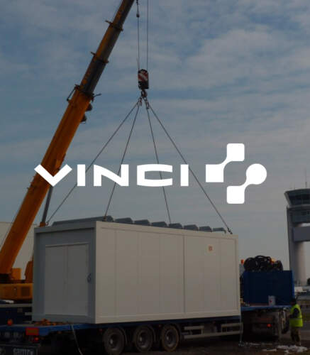 Un conteneur blanc est suspendu par une grue jaune, avec le logo de Vinci en superposition sur un fond nuageux.