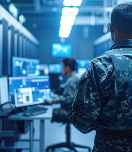 Un militaire de dos surveille des serveurs informatiques dans un centre de données, avec un poste de contrôle en arrière-plan.