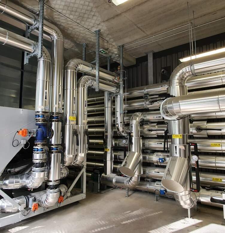 Installation CVC industrielle avec réseaux de tuyauterie isolés, gaines métalliques et équipements techniques dans un local technique.