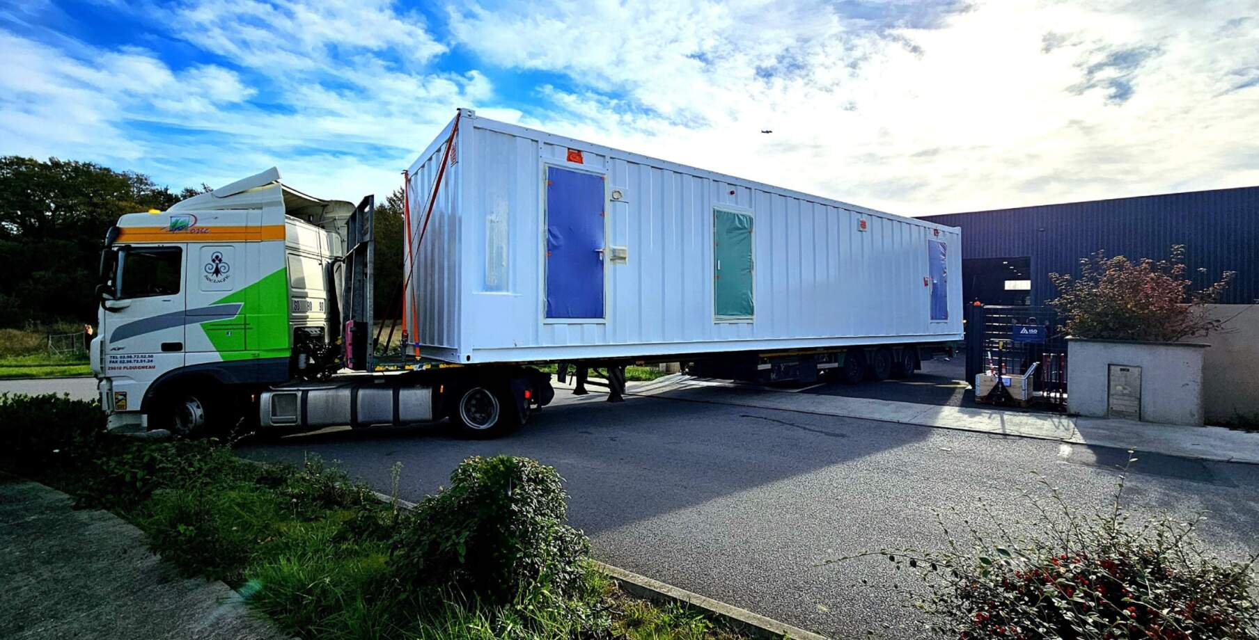 Livraison et installation d’un conteneur technique modulaire sur un site industriel à l’aide d’un camion plateau.