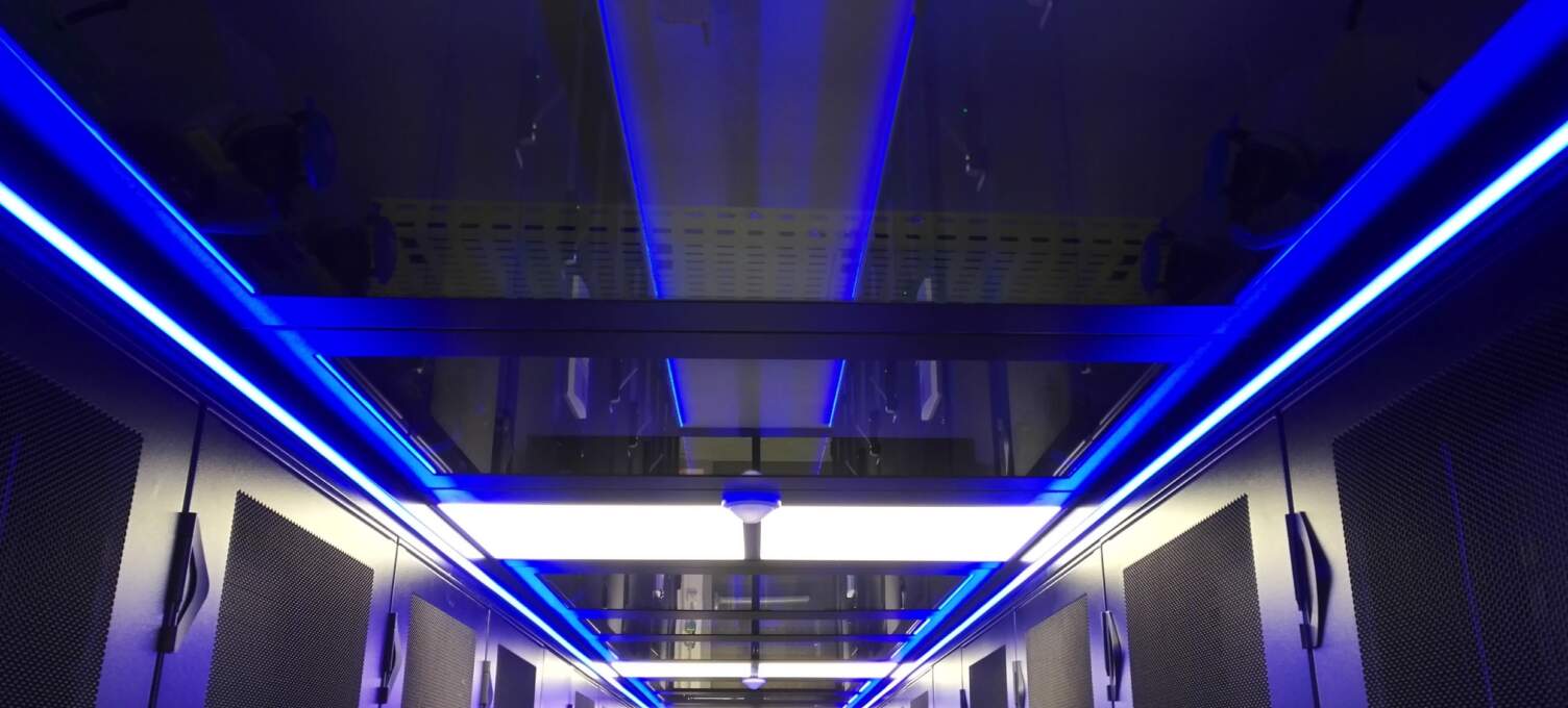 Vue intérieure d'un datacenter avec des allées éclairées en bleu, racks de serveurs sur les côtés et plafond moderne.