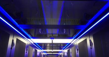 Vue intérieure d'un datacenter avec des allées éclairées en bleu, racks de serveurs sur les côtés et plafond moderne.