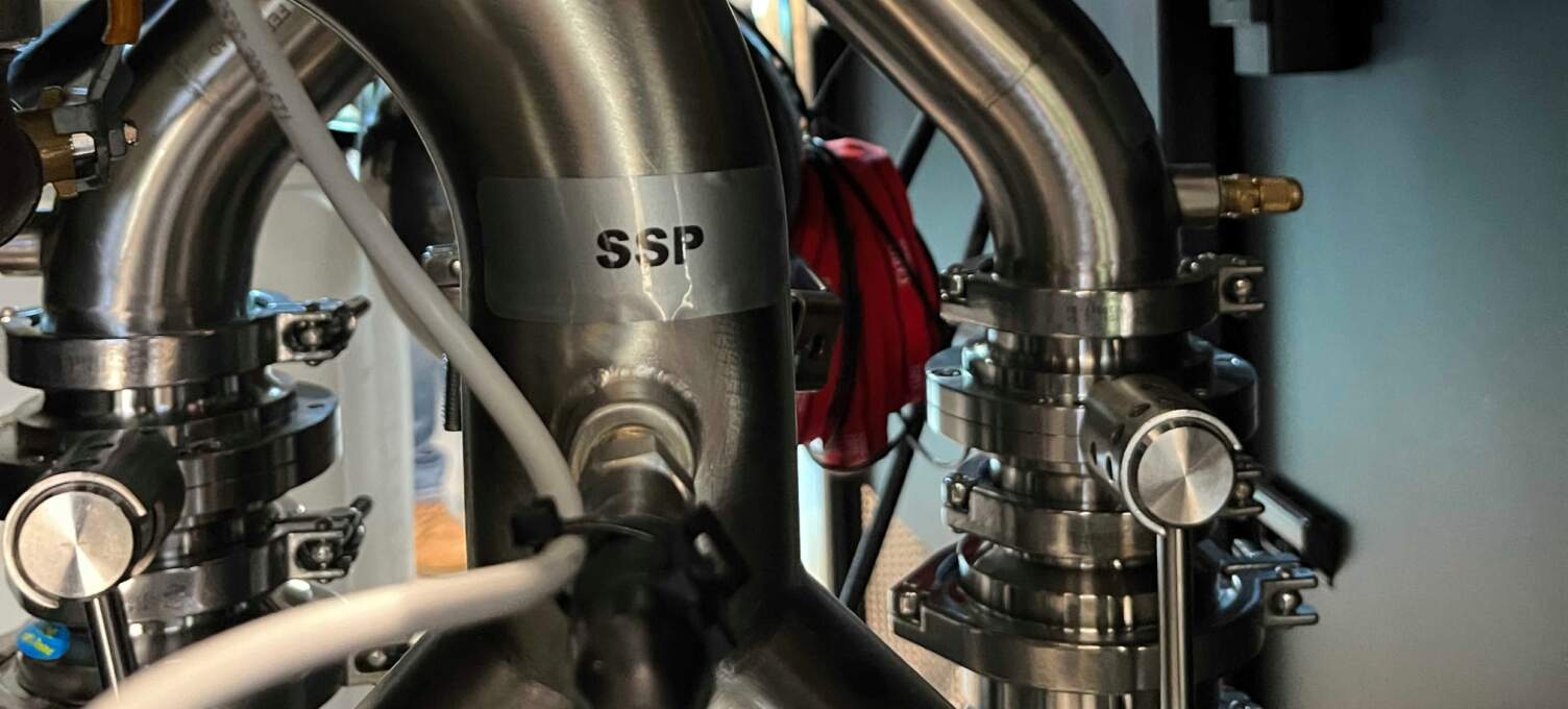 Gros plan sur des tuyaux en acier inoxydable avec des étiquettes, des connexions et des câbles, symbolisant les infrastructures techniques.