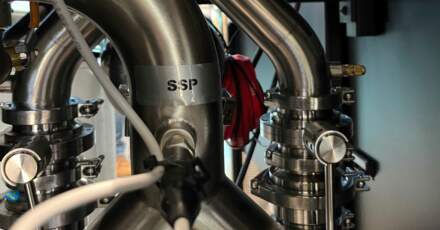 Gros plan sur des tuyaux en acier inoxydable avec des étiquettes, des connexions et des câbles, symbolisant les infrastructures techniques.