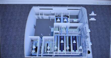 Plan en 3D d'un espace de travail, montrant plusieurs salles avec des équipements, en gris et bleu, sur fond clair.
