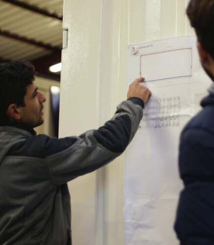 Techniciens examinant un plan technique affiché sur un mur dans un atelier.