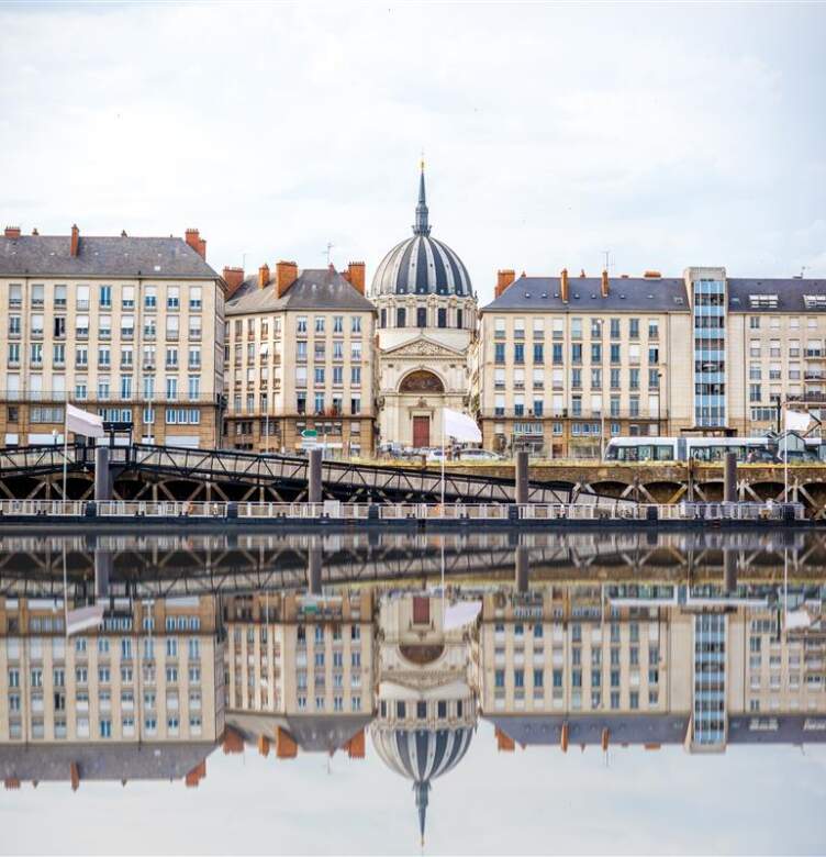 Vue du quai de la Loire à Nantes avec l’église Notre-Dame de Bon-Port et les façades d’immeubles reflétées dans l’eau.