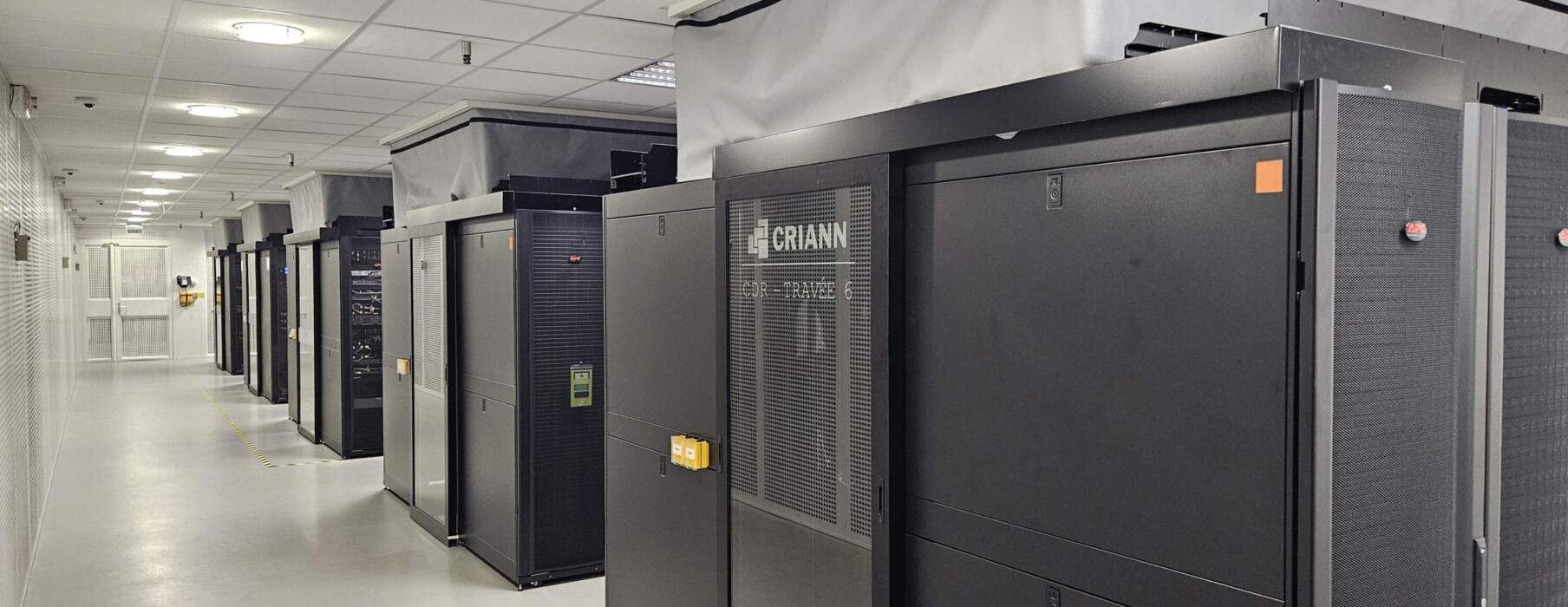 Série de serveurs noirs alignés dans un couloir lumineux, avec des panneaux de sécurité sur le dessus et un sol blanc.