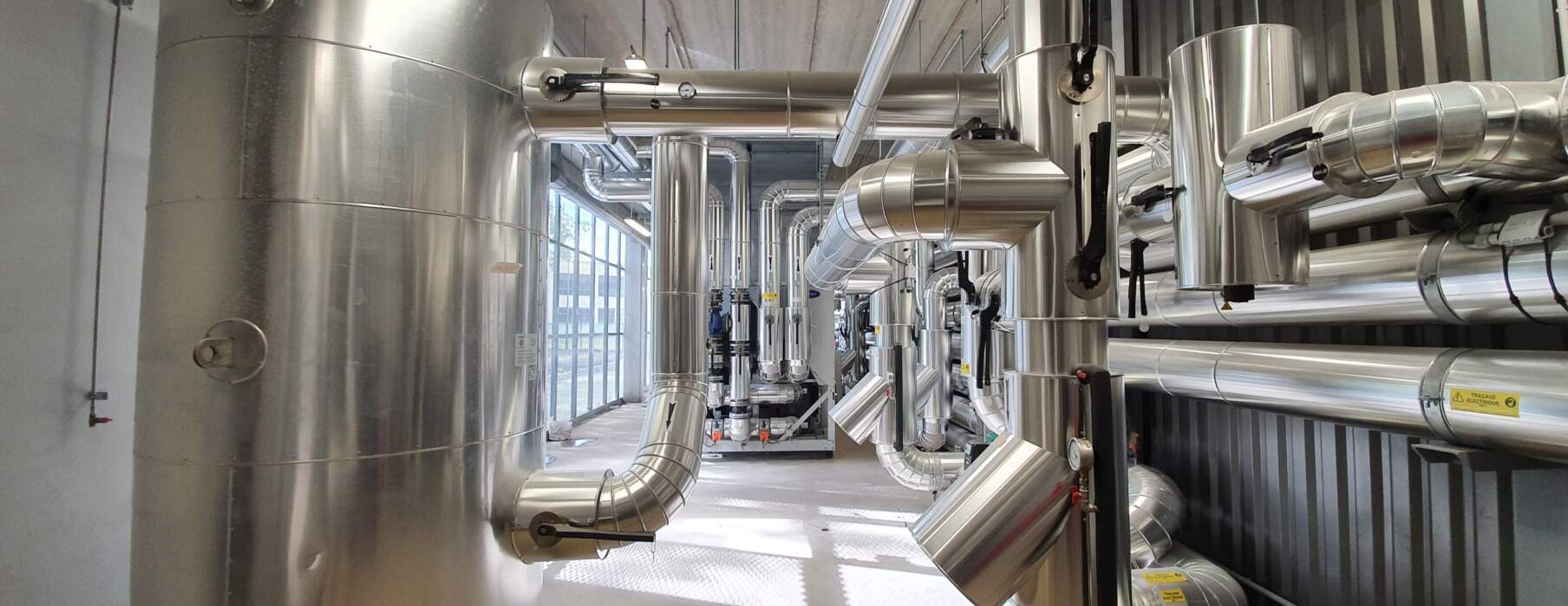 Vue intérieure d'un datacenter avec de grands réservoirs métalliques et des conduits en acier inoxydable, éclairage naturel abondant.