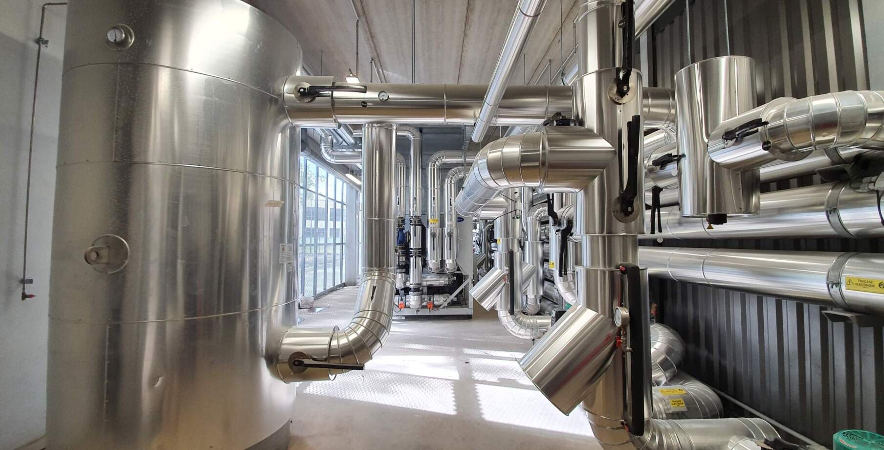 Vue intérieure d'un datacenter avec de grands réservoirs métalliques et des conduits en acier inoxydable, éclairage naturel abondant.