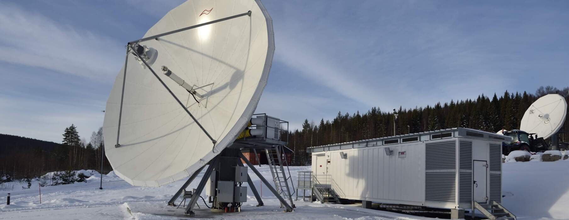 Un centre de données modulaire dans la neige, avec une grande antenne parabolique et un bâtiment aux parois blanches, entouré d'arbres.
