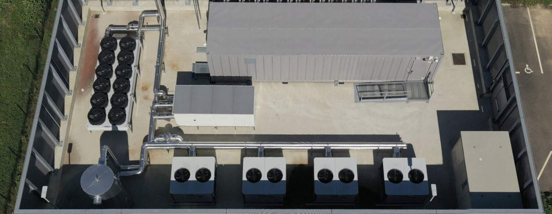 Un module technique préfabriqué est soulevé par une grue au-dessus d’une zone arborée, avec en arrière-plan la skyline d’un quartier d’affaires.