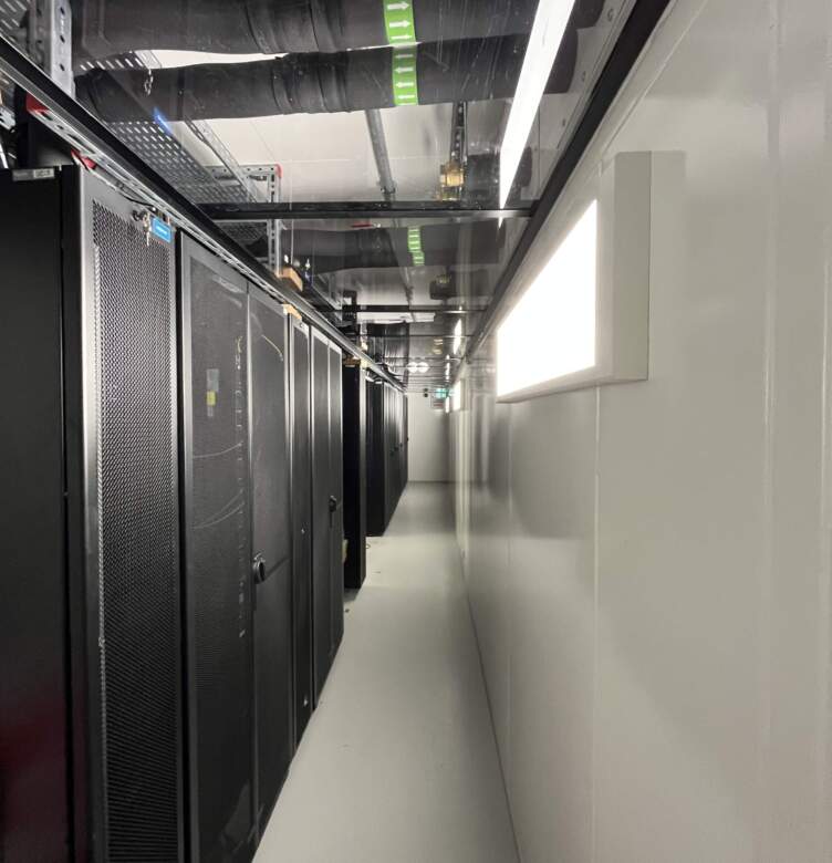 Allée d'un datacenter, avec des armoires noires alignées, éclairage LED au plafond et conduits noirs visibles. Éurocher minimaliste.