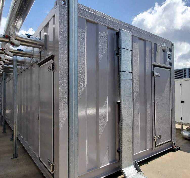 Vue extérieure d’installations techniques sur un toit, avec modules métalliques, portes de maintenance et tuyauteries industrielles sous un ciel nuageux.