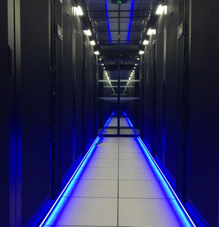 A hallway in a modern data center featuring black server racks and blue LED lighting, creating a high-tech atmosphere.