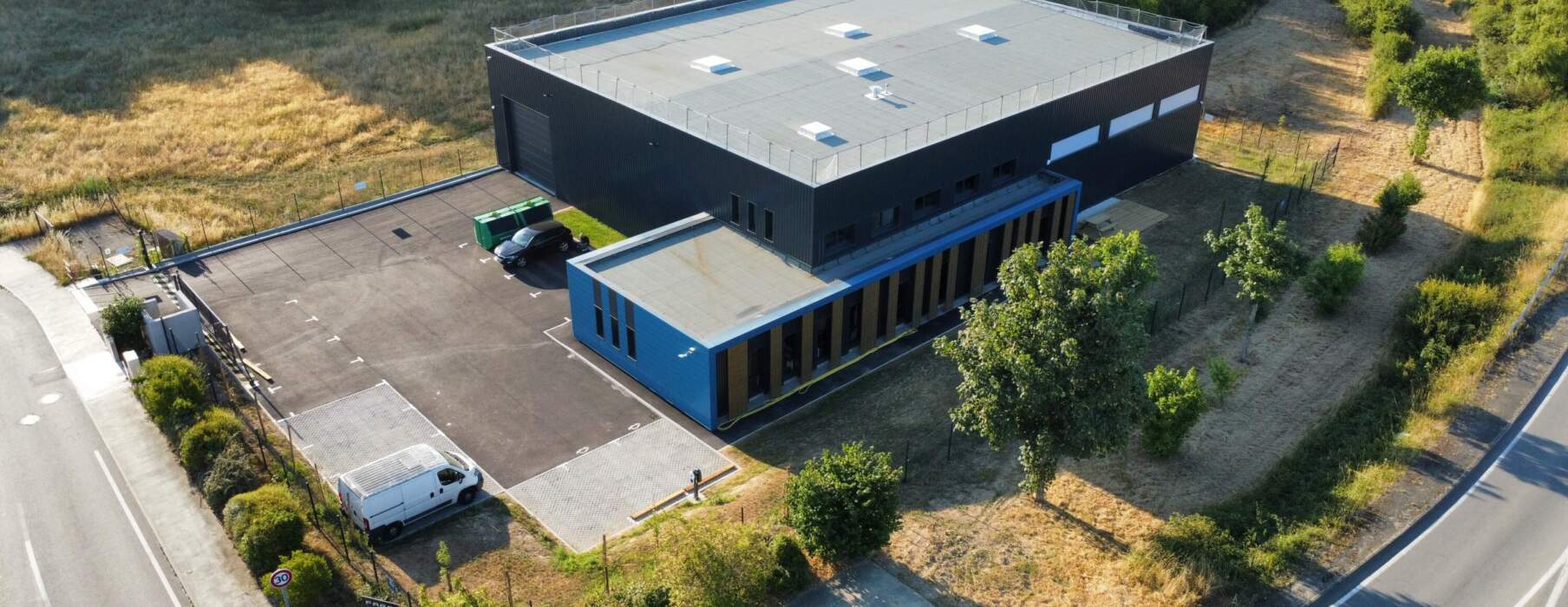 Aerial view of a modern data center building with a gray roof and black and blue walls, surrounded by greenery and well-maintained grounds.