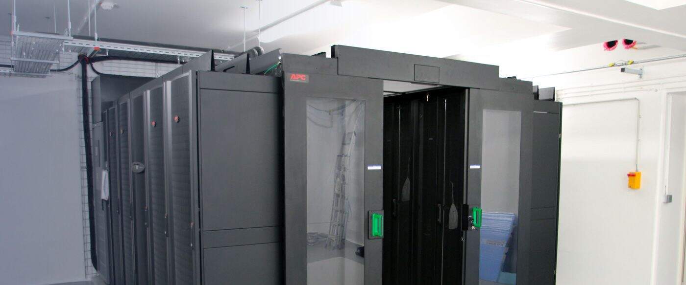 Black server system with glass doors, installed in a well-lit server room, with visible cabling on the ceiling.