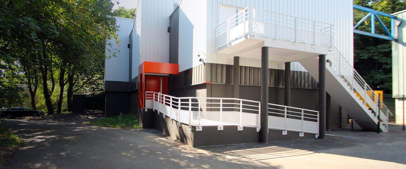 Bâtiment moderne de l'Université de Nantes, avec un accès en rampes, des murs gris et orange, et des arbres en arrière-plan.