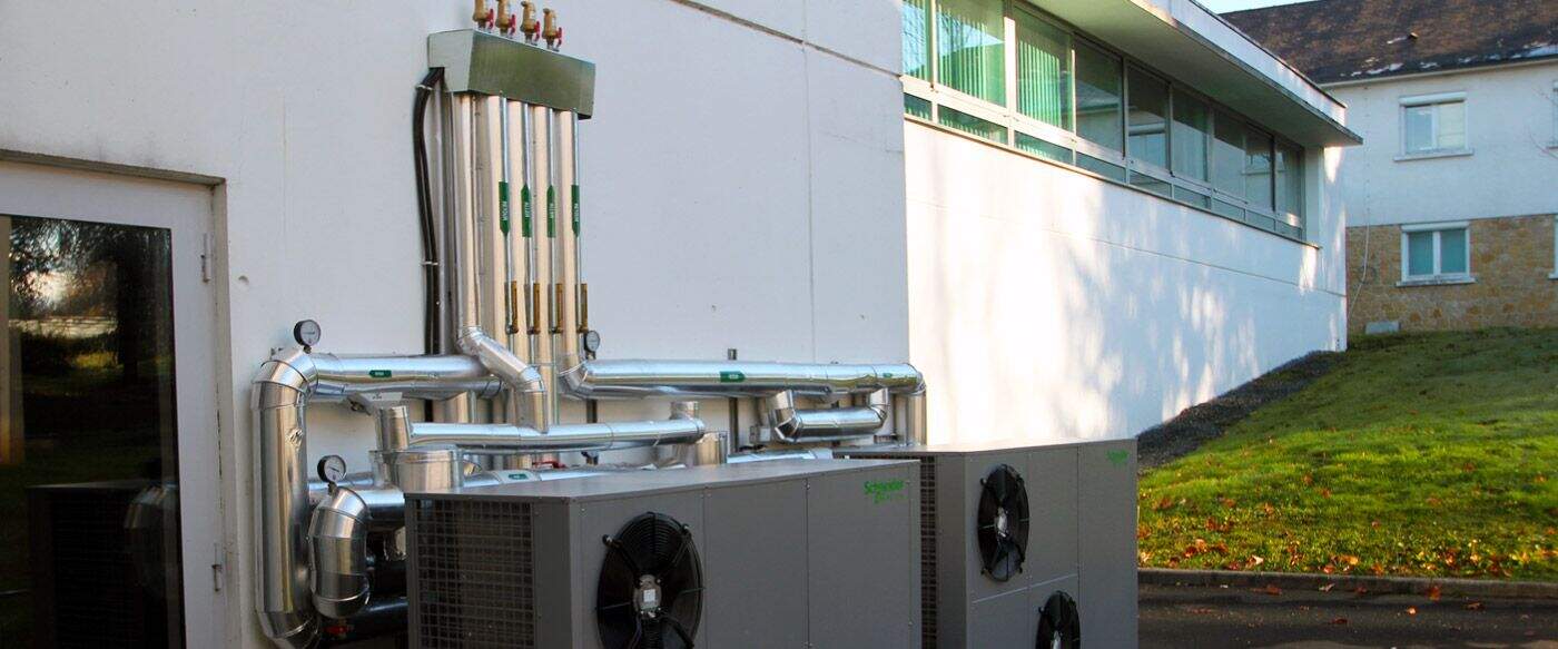 Système de climatisation installé sur un mur extérieur blanc, avec plusieurs conduits métalliques et compresseurs gris.