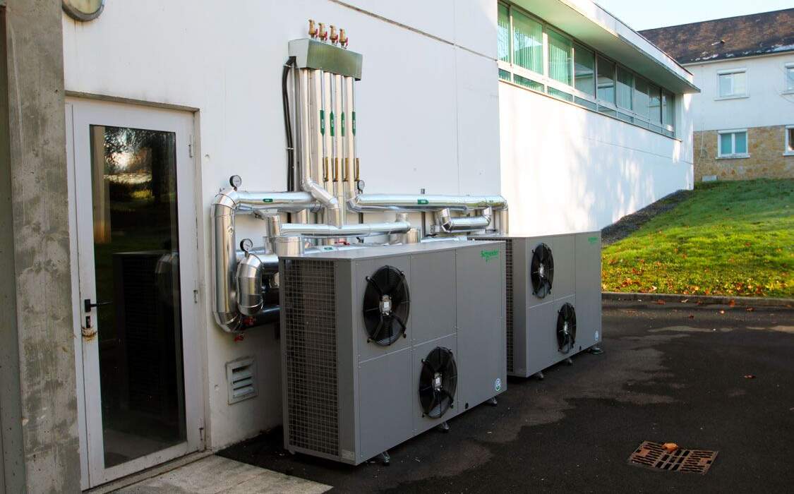 Système de climatisation installé à l'extérieur d'un bâtiment, avec des unités grises et des tuyaux métalliques en acier inoxydable.